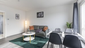 A modern living room with a grey sofa, a round coffee table, and a dining area with a white table and black chairs.