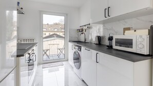A modern kitchen with white cabinets, a built-in oven, a microwave, and a washing machine.