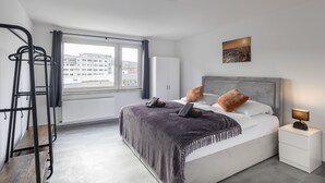 A modern bedroom with a bed, bedside table, and a view of buildings through a window.