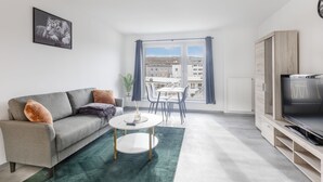 A modern living room with a grey sofa, a round coffee table, a TV on a wooden stand, and a dining area with a table and chairs.