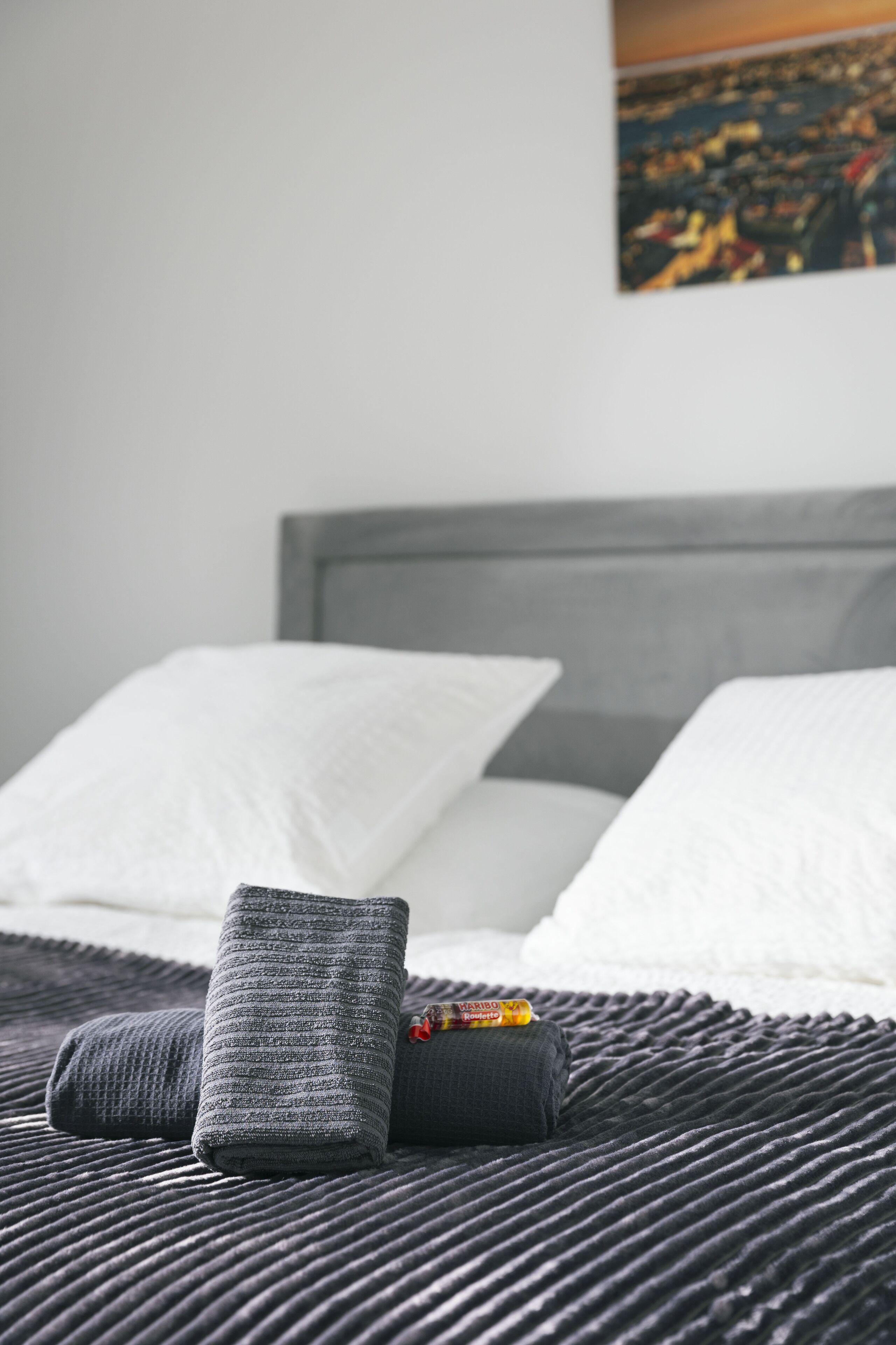 Una cama con ropa de cama gris y blanca, un almohadón gris con textura y una manta negra texturizada.
