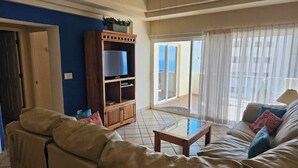 Una sala de estar con sofá, una mesa de centro, un mueble para televisión y una puerta corrediza de vidrio que da a un balcón.