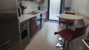 A compact kitchen with a washing machine, a sink, and a stove. There is a dining area with a table and chairs.