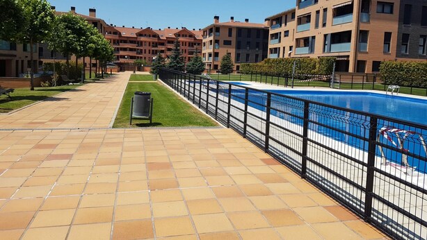 A residential area with a swimming pool, tiled walkways, and apartment buildings.