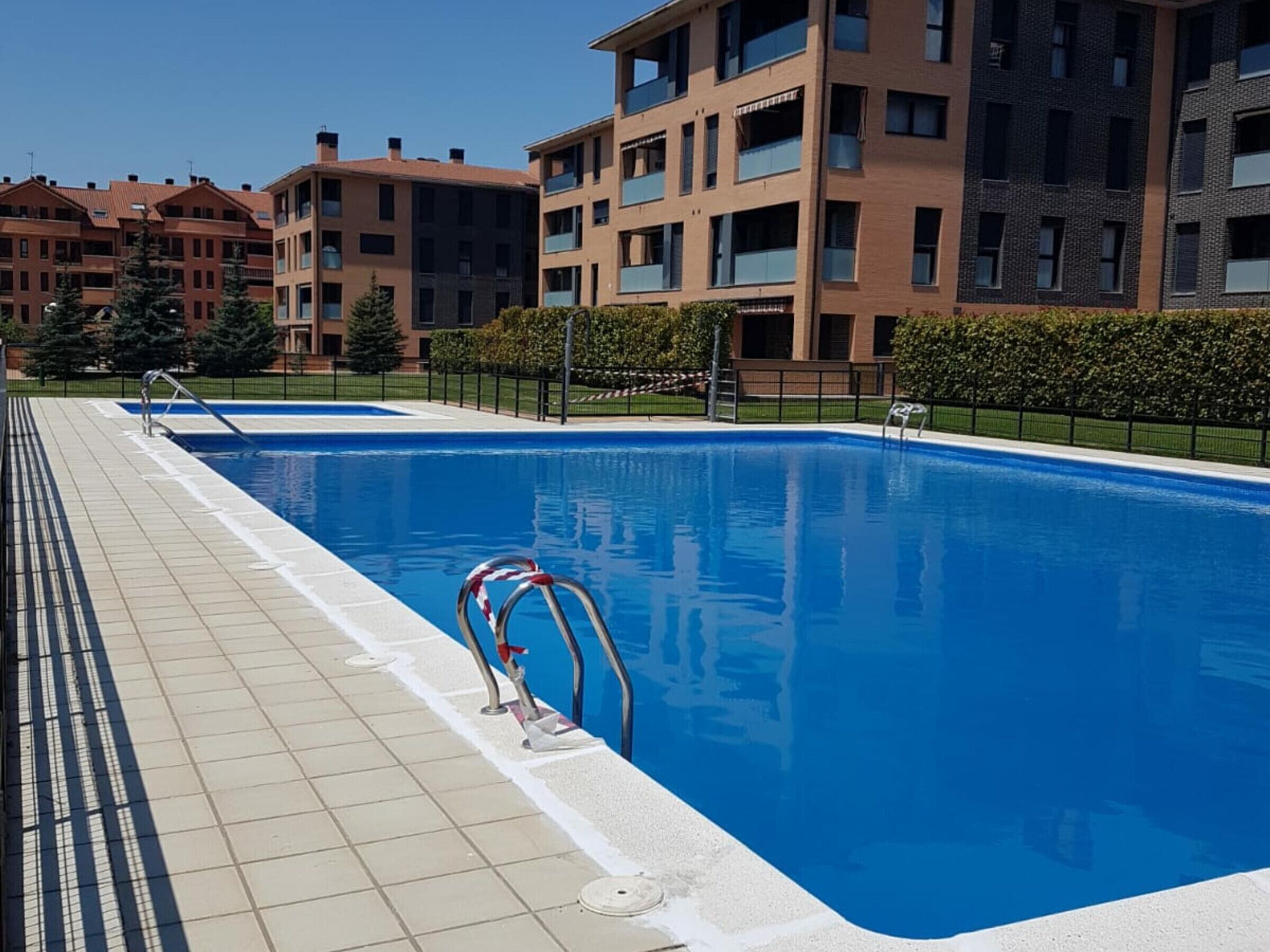 A swimming pool with a tiled deck, surrounded by apartment buildings.