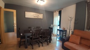 A living room with a dining table, chairs, a sofa, a floor lamp, and a coat rack.