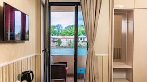 A balcony with a view of a river, a television mounted on the wall, and a wicker chair. - hotel sanapiro (Kutaisi)
