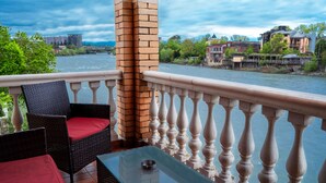 A balcony with wicker chairs and a table, overlooking a river with buildings in the background. - hotel sanapiro (Kutaisi)