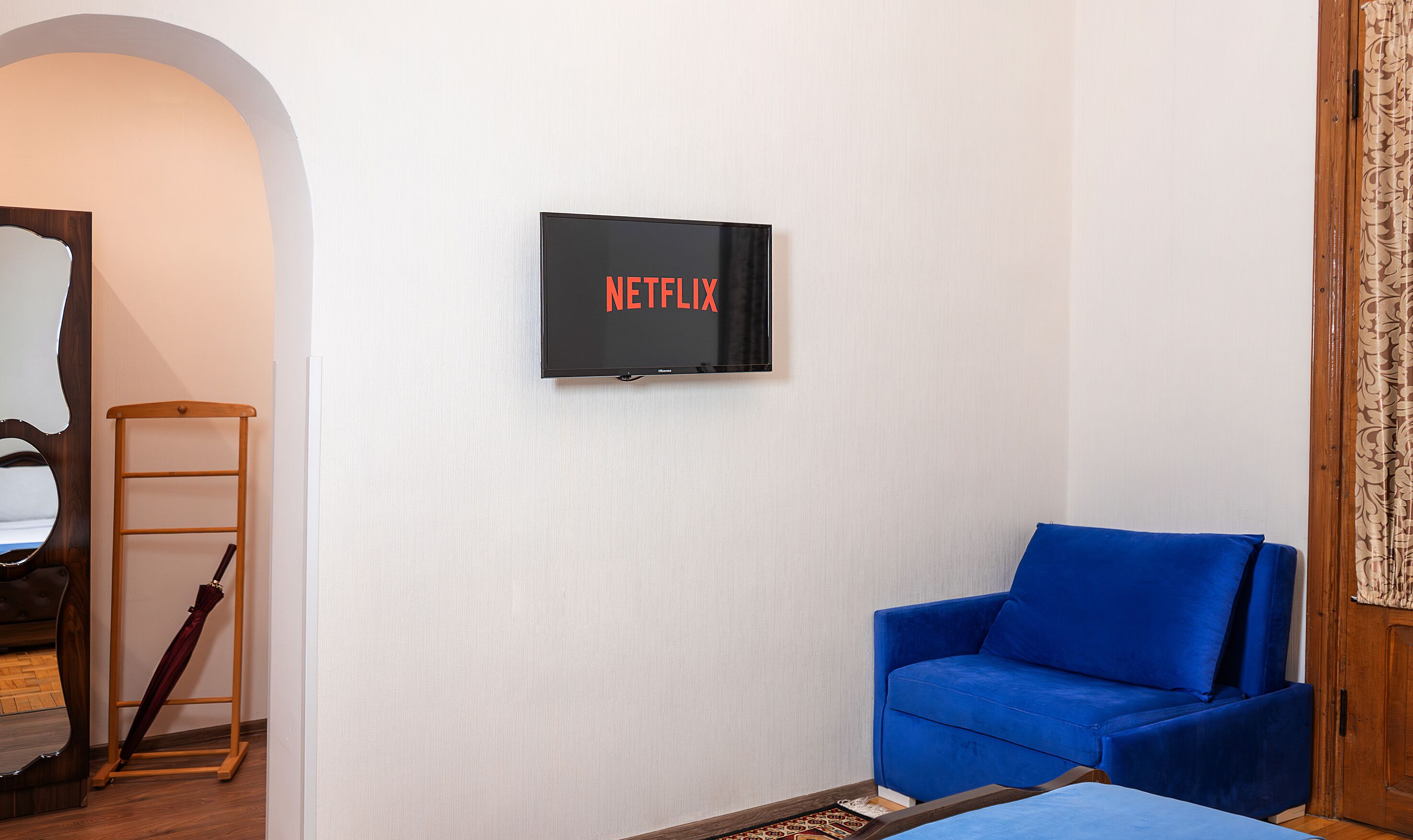 Habitación con una televisión de montaje, el logotipo de Netflix, un sofá azul, una escalera de madera y piso de madera.