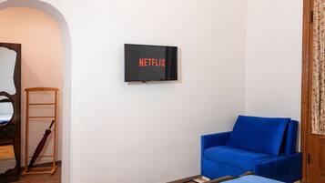 Habitación con una televisión de montaje, el logotipo de Netflix, un sofá azul, una escalera de madera y piso de madera.