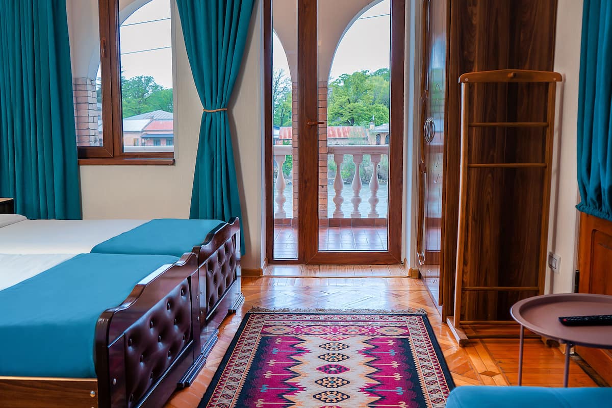 A hotel room with a bed, a small table, a rug, and a view of the outside.