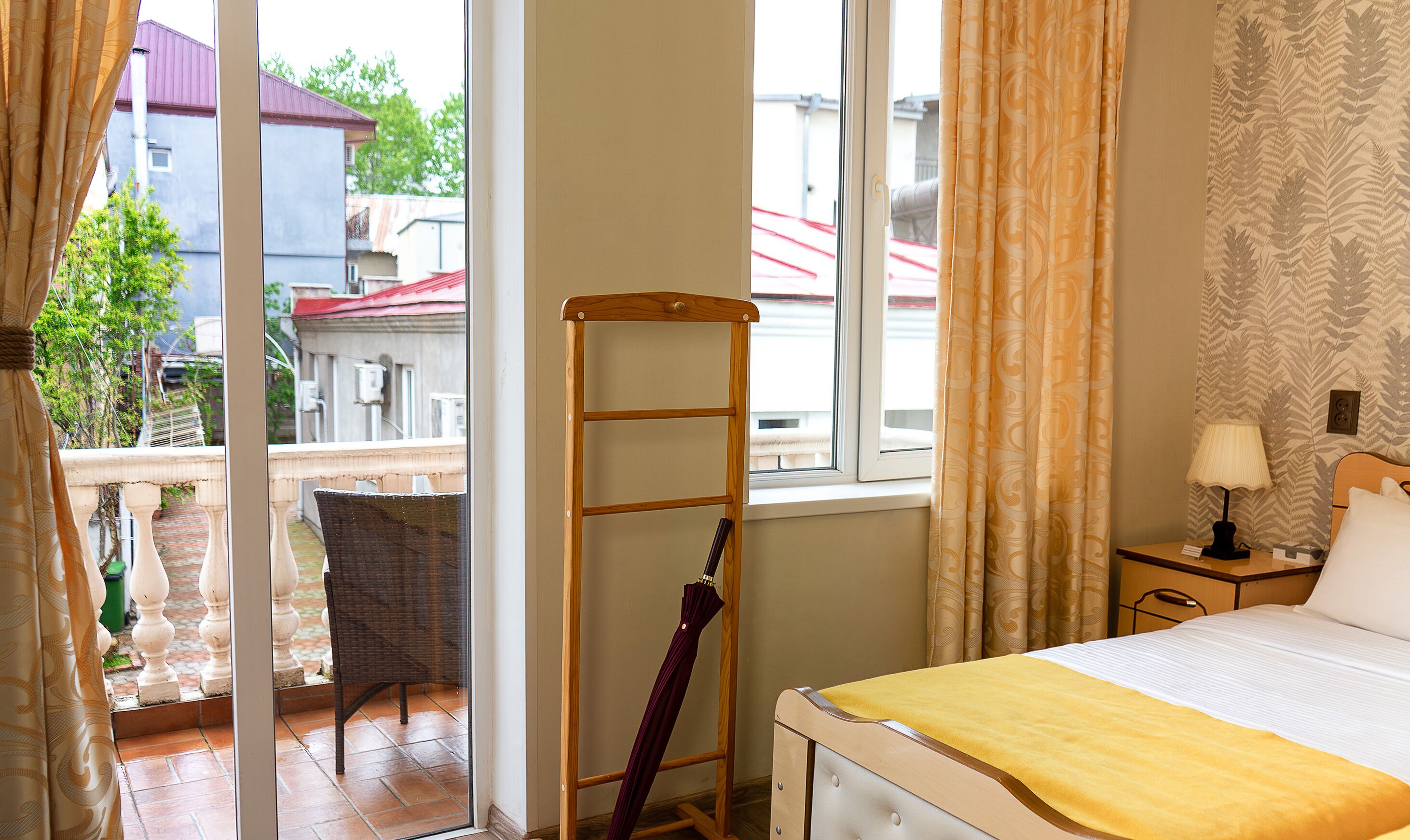 Quarto de hotel com cama, mesa de cabeceira, luminária, escada de madeira e vista para a varanda externa.