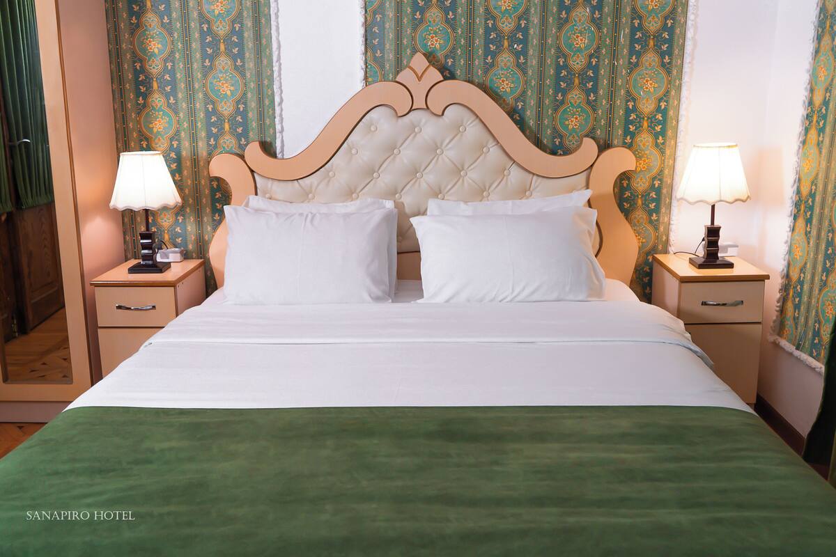 A hotel room with a large bed, two bedside tables with lamps, and patterned curtains.