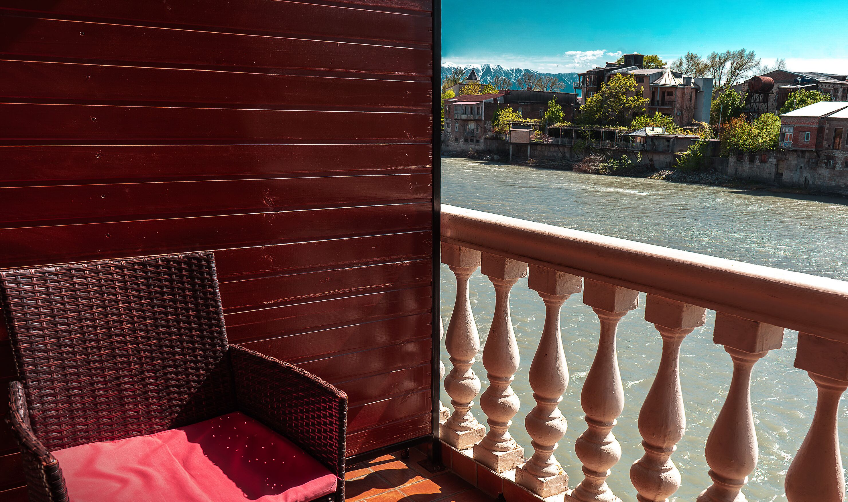 Un balcon en bois avec une chaise en osier et un coussin rouge.