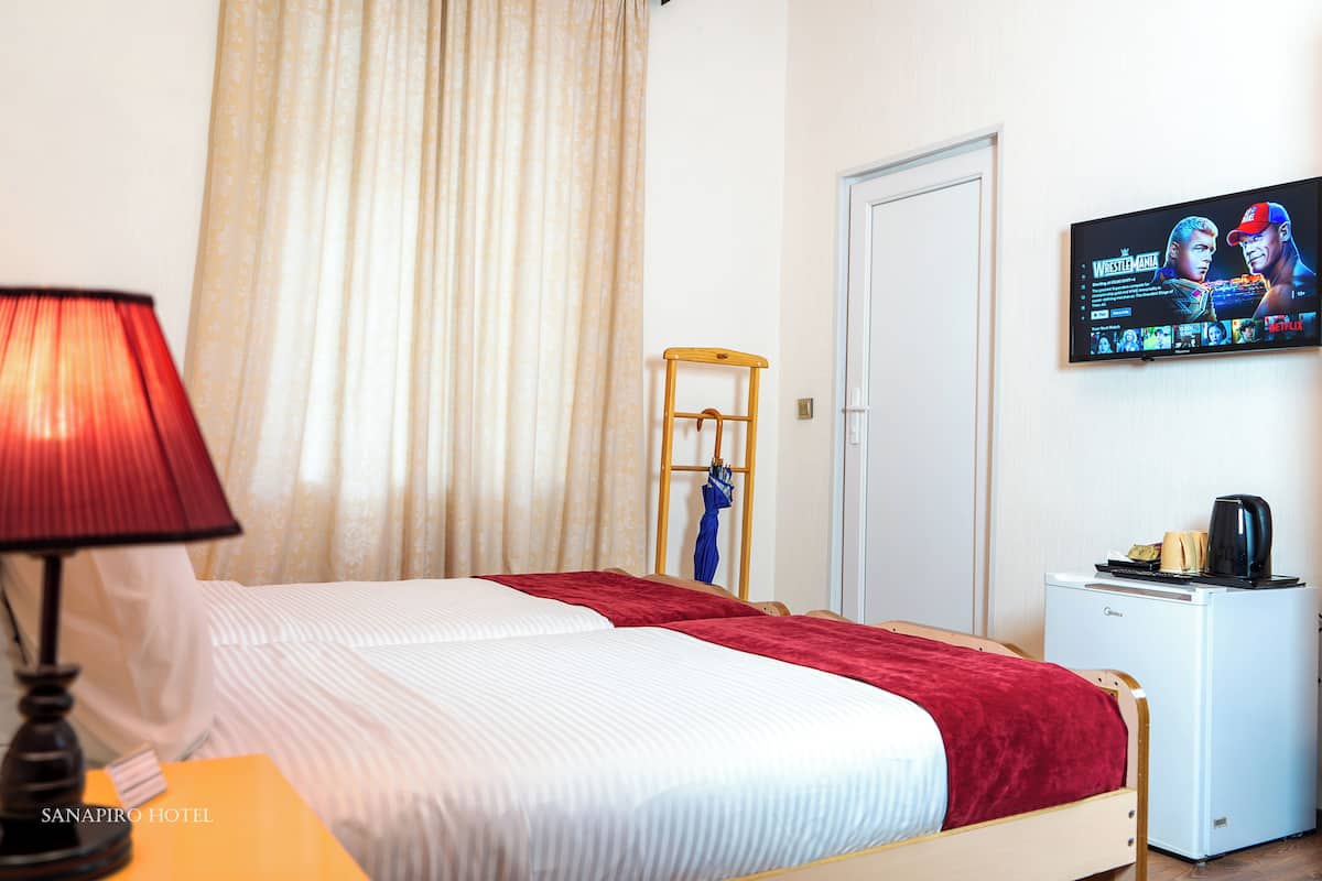 A hotel room with a bed, a TV on the wall, a desk with a lamp, and a small refrigerator.