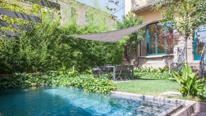 A swimming pool surrounded by lush greenery and a building with a balcony. - Antigua Fábrica Descals, Edificio Histórico (Olot)