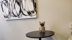 Eine kleine, moderne Küche mit einem runden Tisch, zwei Barhocker, einem Blumentopf und einem großen abstrakten Gemälde an der Wand.