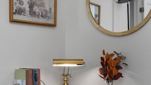 Ein Holztisch mit einer Lampe, Büchern, einer Blumenvase, einem gerahmten Bild und einem runden Spiegel.