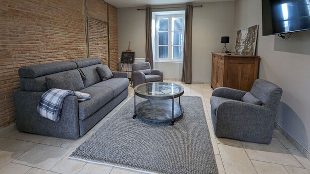 Un salon avec un mur en briques, un canapé, une table basse et un téléviseur fixé au mur.