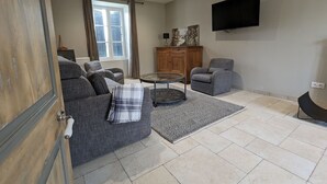 Un salon comprenant un ensemble de canapés, une table basse, un fauteuil gris, un meuble en bois et un téléviseur à écran plat fixé au mur.