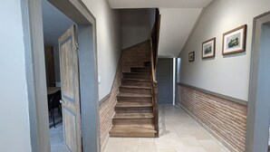 Un couloir avec un escalier en bois, un sol carrelé et des tableaux encadrés accrochés au mur.