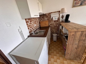 A compact kitchen with a sink, a washing machine, and a small trash bin. - Studio + Cabin with Parking and Terrace - Beach Access (Port Camargue)