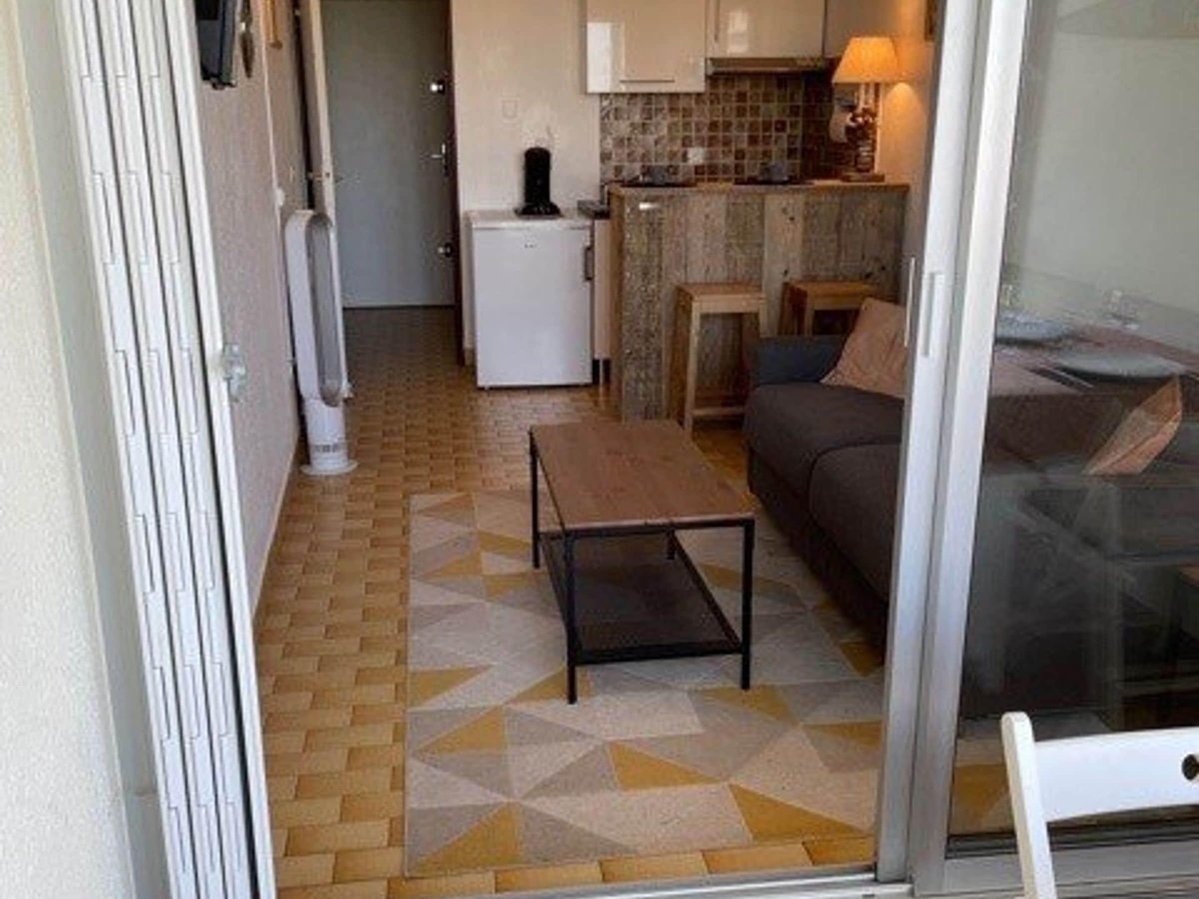 A compact living space with a kitchenette, a sofa, a small table, and a patterned floor.