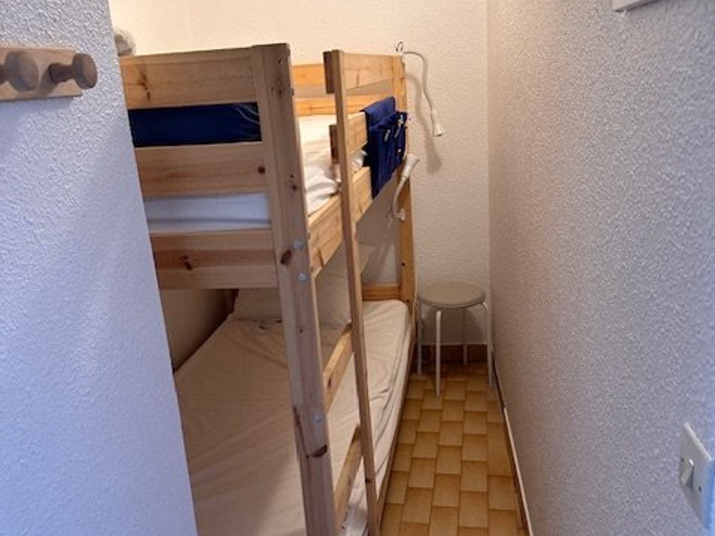 A small, narrow room with a bunk bed and a small stool.