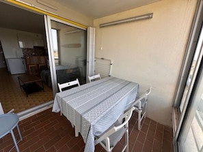 A small balcony with a table and chairs, a sliding glass door leading to a kitchen, and a view of the outside. - Studio + Cabin with Parking and Terrace - Beach Access (Port Camargue)