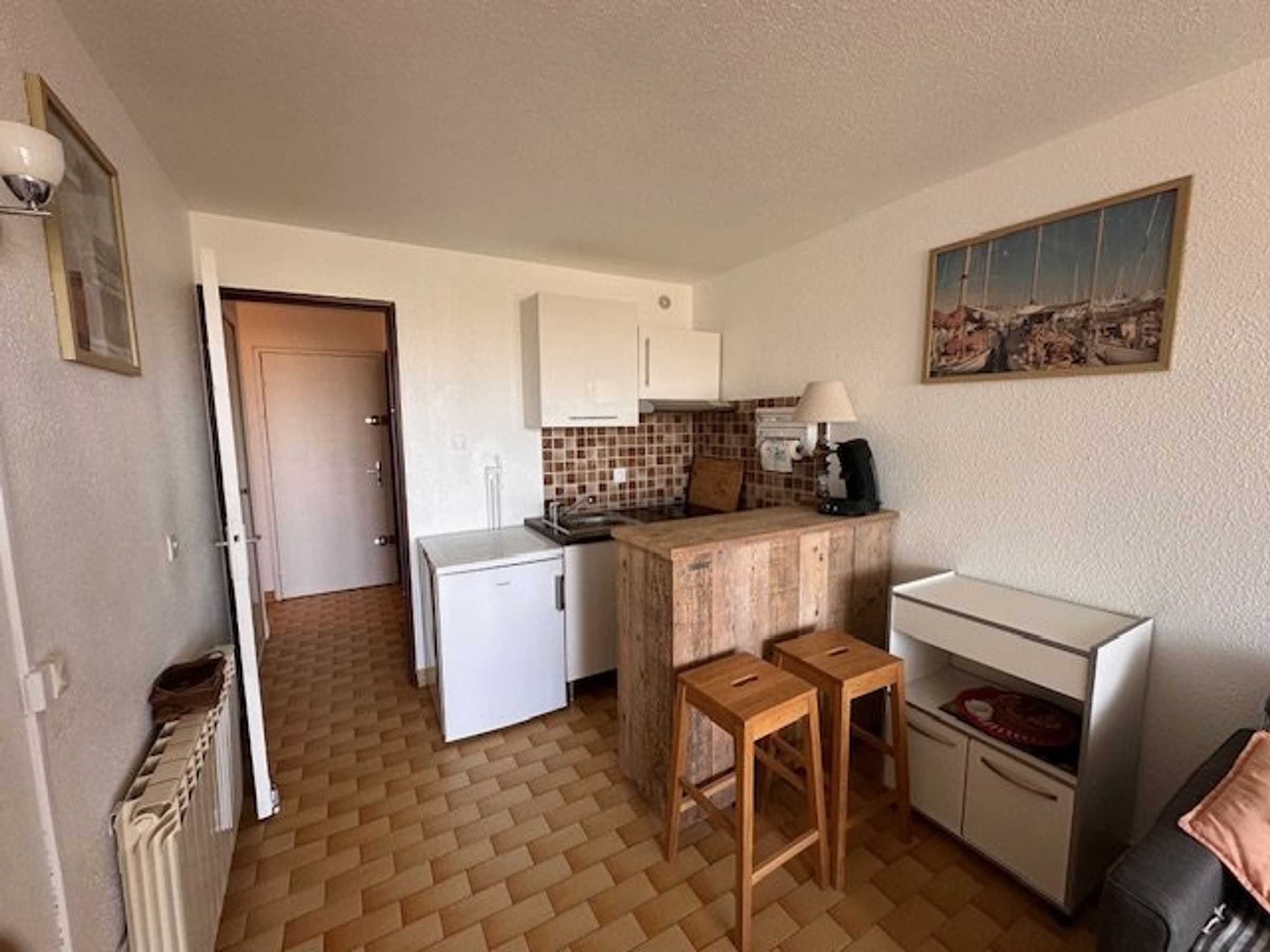 Una cocina compacta con refrigerador, pileta, taburetes de madera y una pequeña mesada.
