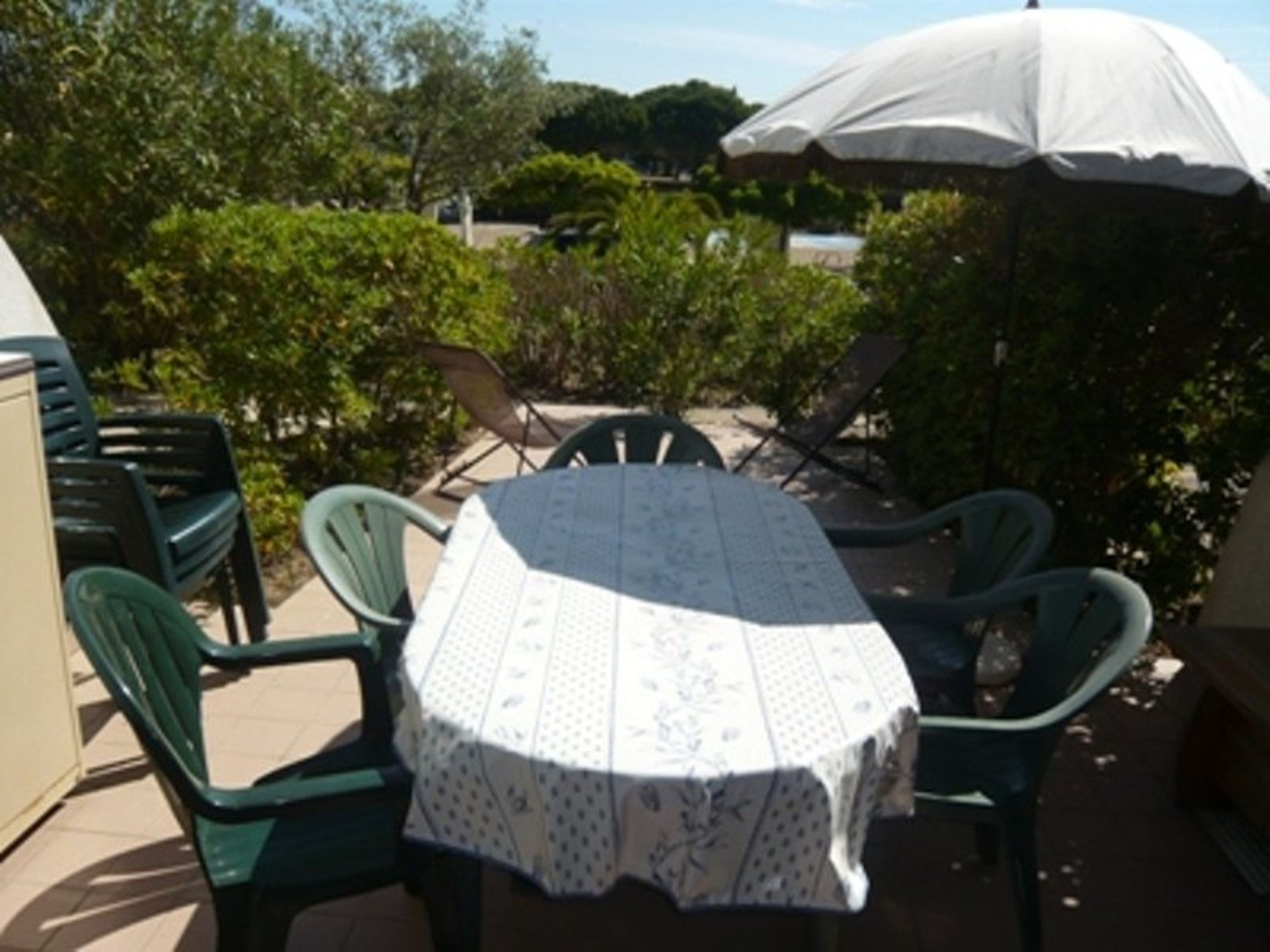 An outdoor patio with a round table and chairs, covered by a white umbrella.