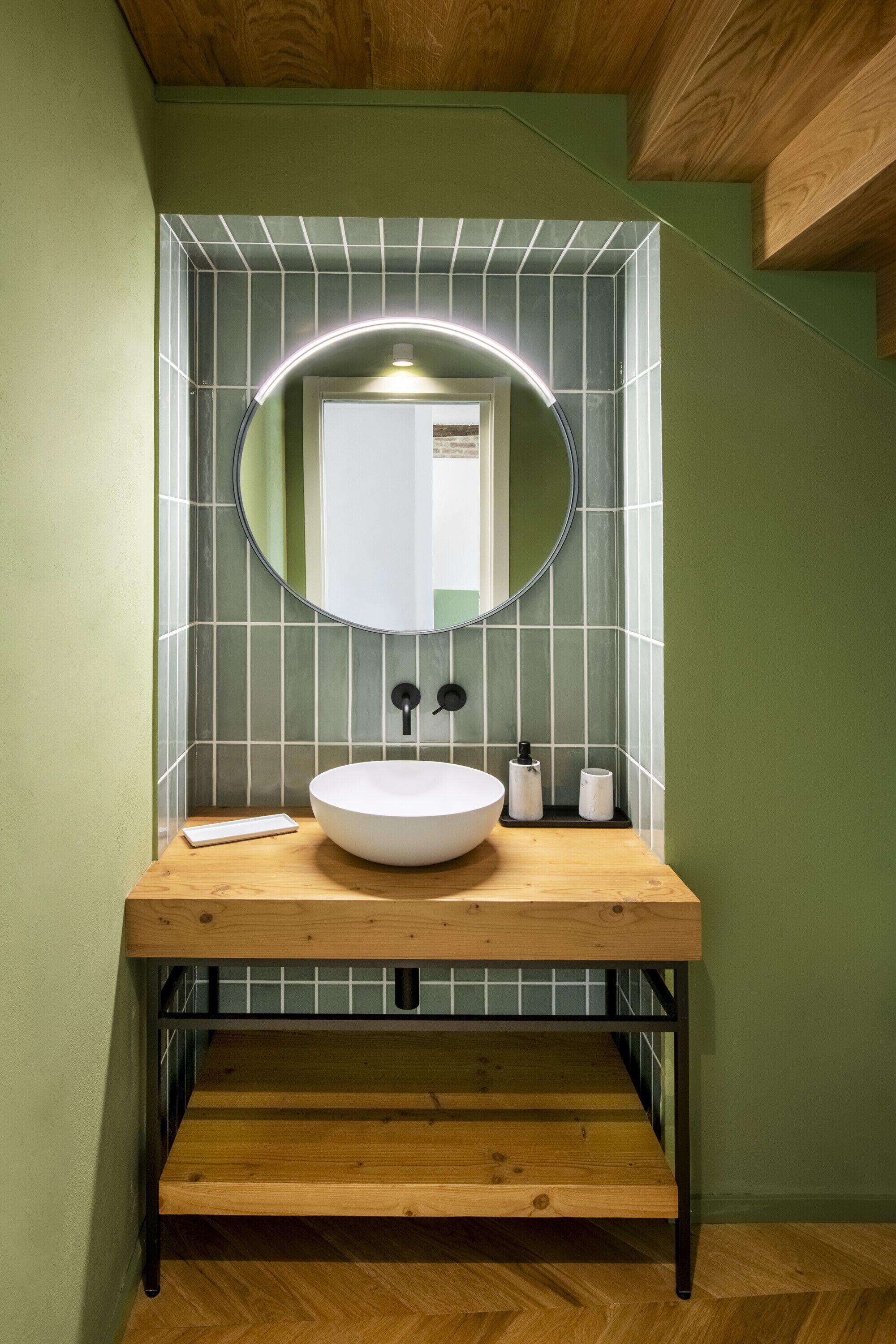 A bathroom with a wooden vanity, a round mirror with a light, and a white sink.