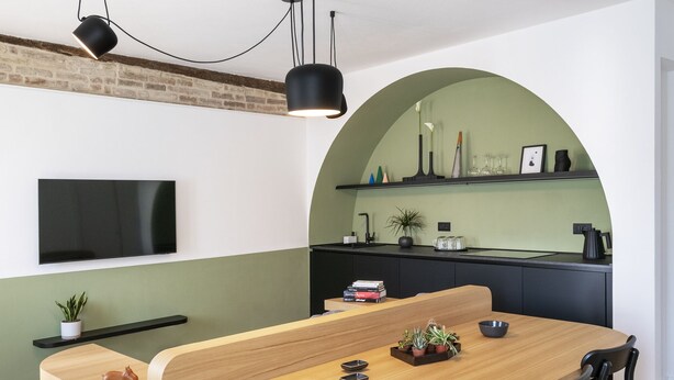 A modern dining area with a wooden table, black chairs, and a TV mounted on the wall.