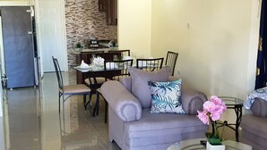 Uma sala de estar moderna com um sofá, uma mesa de centro de vidro e uma área de jantar com uma mesa e cadeiras.
