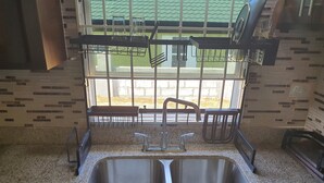 Uma cozinha com uma pia dupla, uma janela com vista para um telhado verde e uma estante de metal acima da pia.