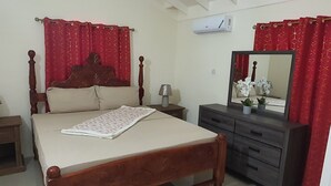 Quarto com cama de madeira, penteadeira, espelho e cortinas vermelhas.