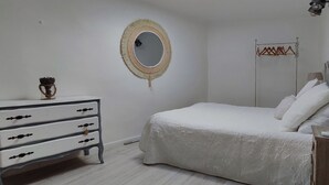 Ein Schlafzimmer mit Bett, Kommode, Spiegel und einer Wandkleiderstange.