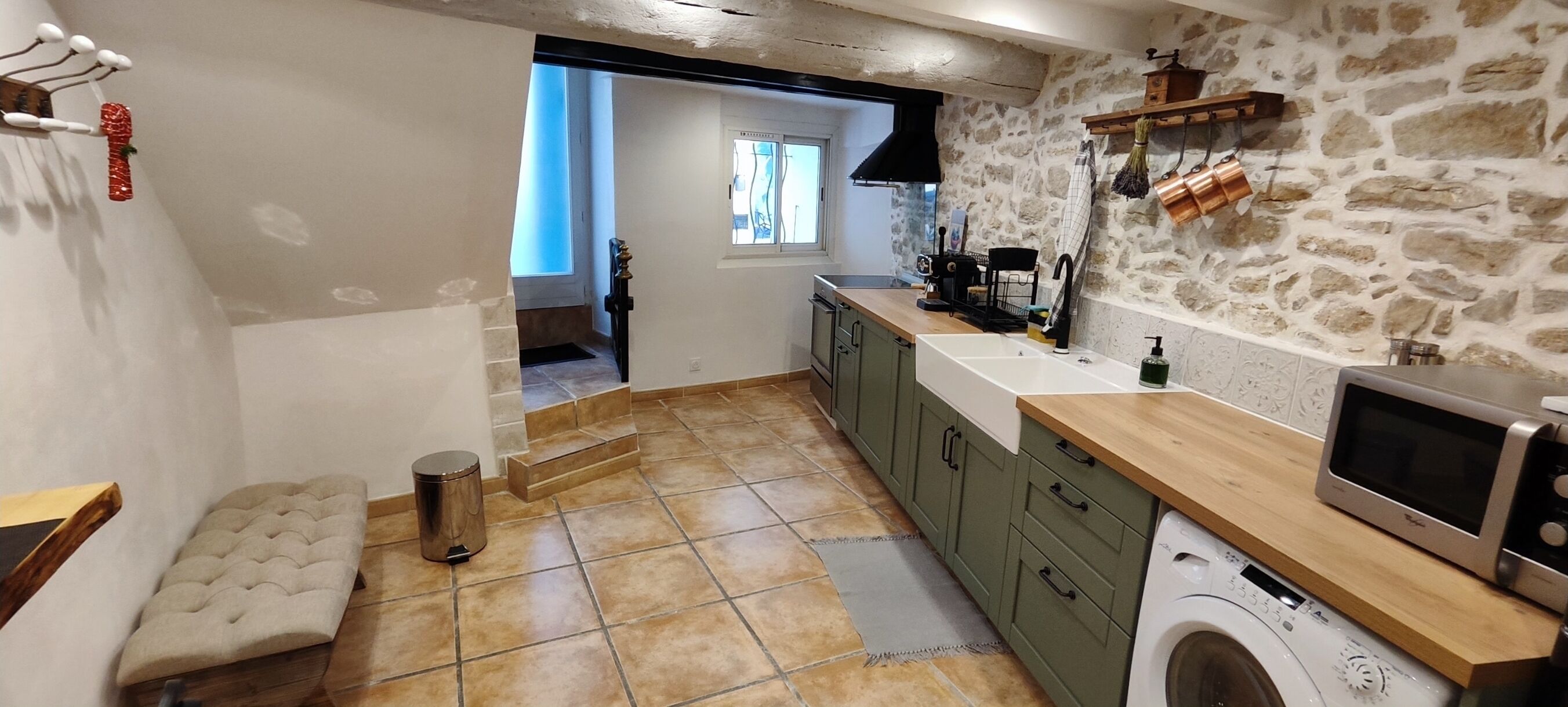 A compact kitchen with a washing machine, a microwave, and a stone wall.