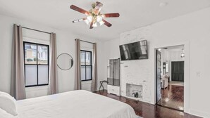A modern bedroom with a large bed, a ceiling fan, a TV, and a fireplace. - Cozy Duplex Near DT, King, 3 TVs, Walk To Dine (Columbia)