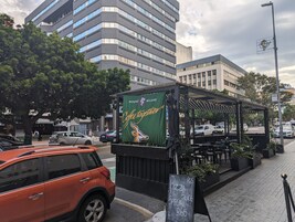 Un café a la calle con mesas al aire libre, un menú en pizarra y un cartel verde que anuncia café.