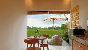 A dining area with a table, chairs, and a large umbrella. A kitchen area is visible to the right. - Uma Rimbun Villa by Dhananjaya Hospitality (Ubud)