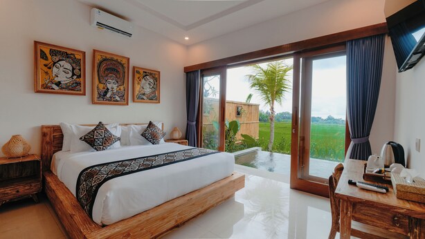 A bedroom with a large bed, a wooden headboard, a dining table with chairs, and a view of a green landscape through large sliding doors. - Uma Rimbun Villa by Dhananjaya Hospitality (Ubud)