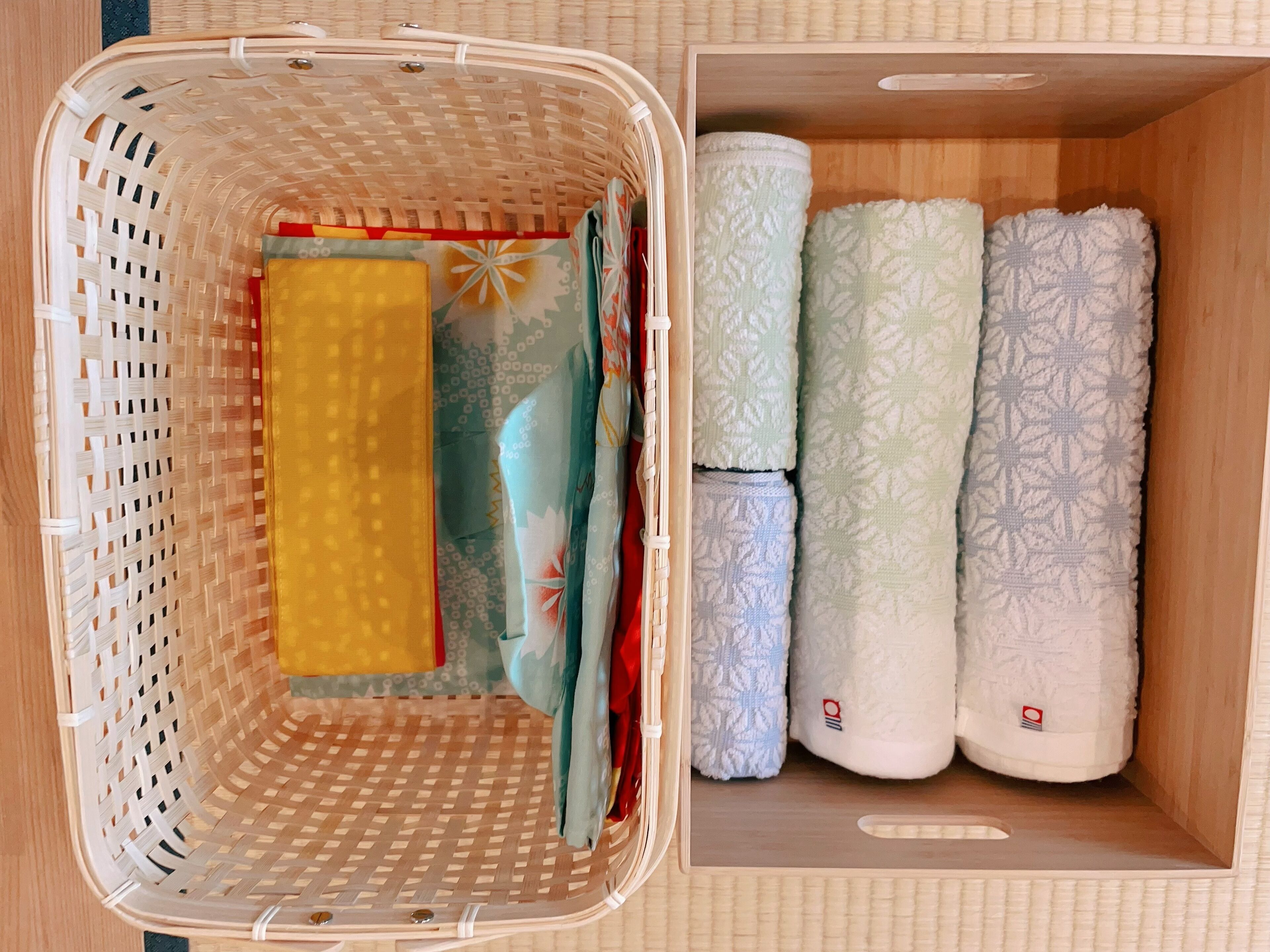 A wicker basket with folded towels and a rolled-up blanket inside a wooden box.