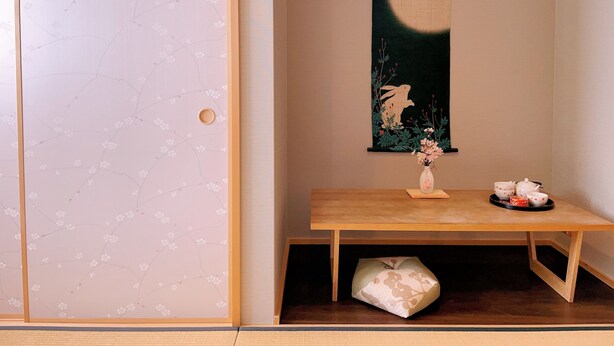 A traditional Japanese room with a sliding door, a wooden table with a vase of flowers, and a hanging artwork depicting a moon and a bird. - suikakan heianjingumae (Kyoto)