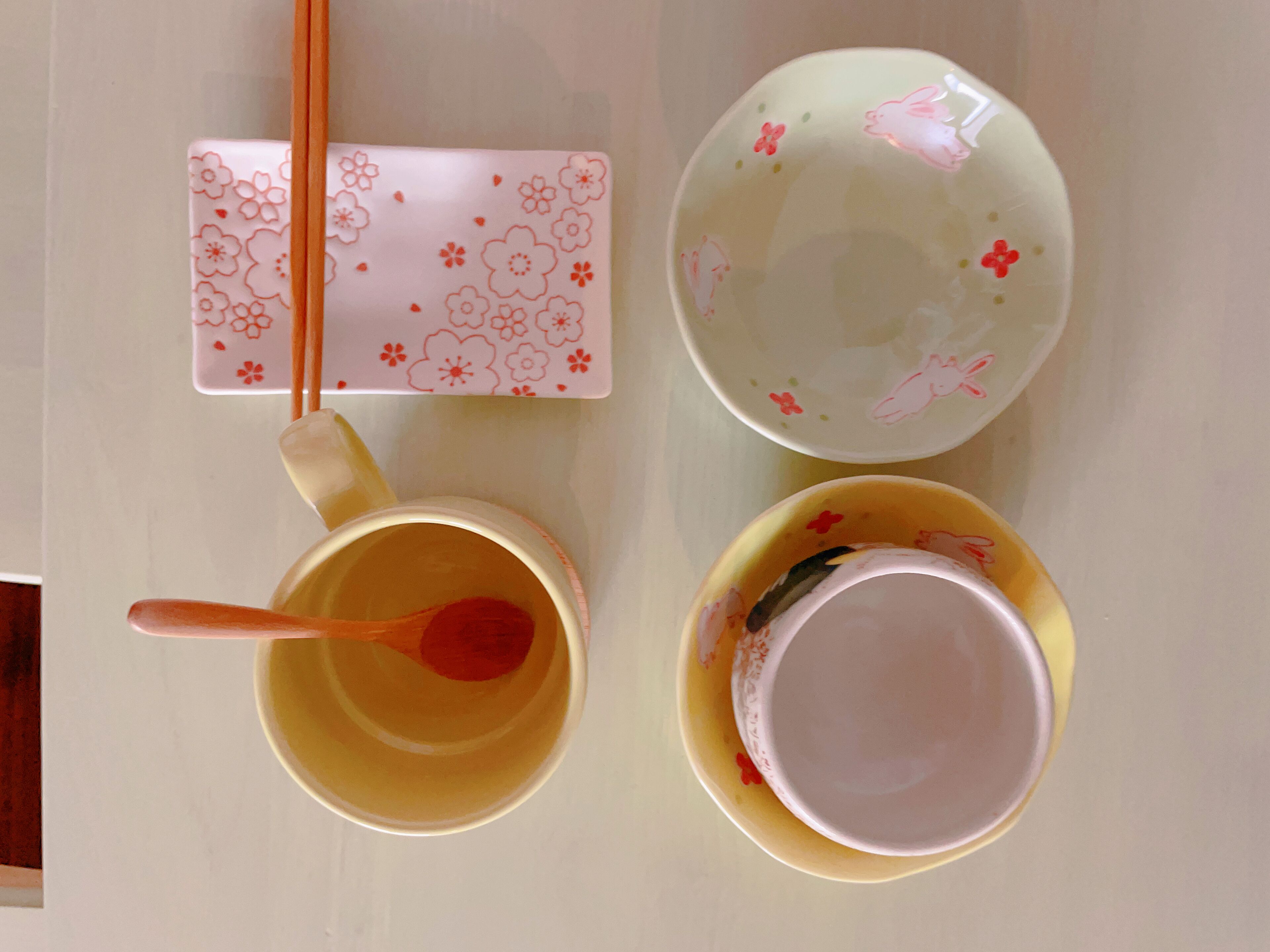 A table with a pair of chopsticks, a teapot, and two cups, one with a floral pattern.