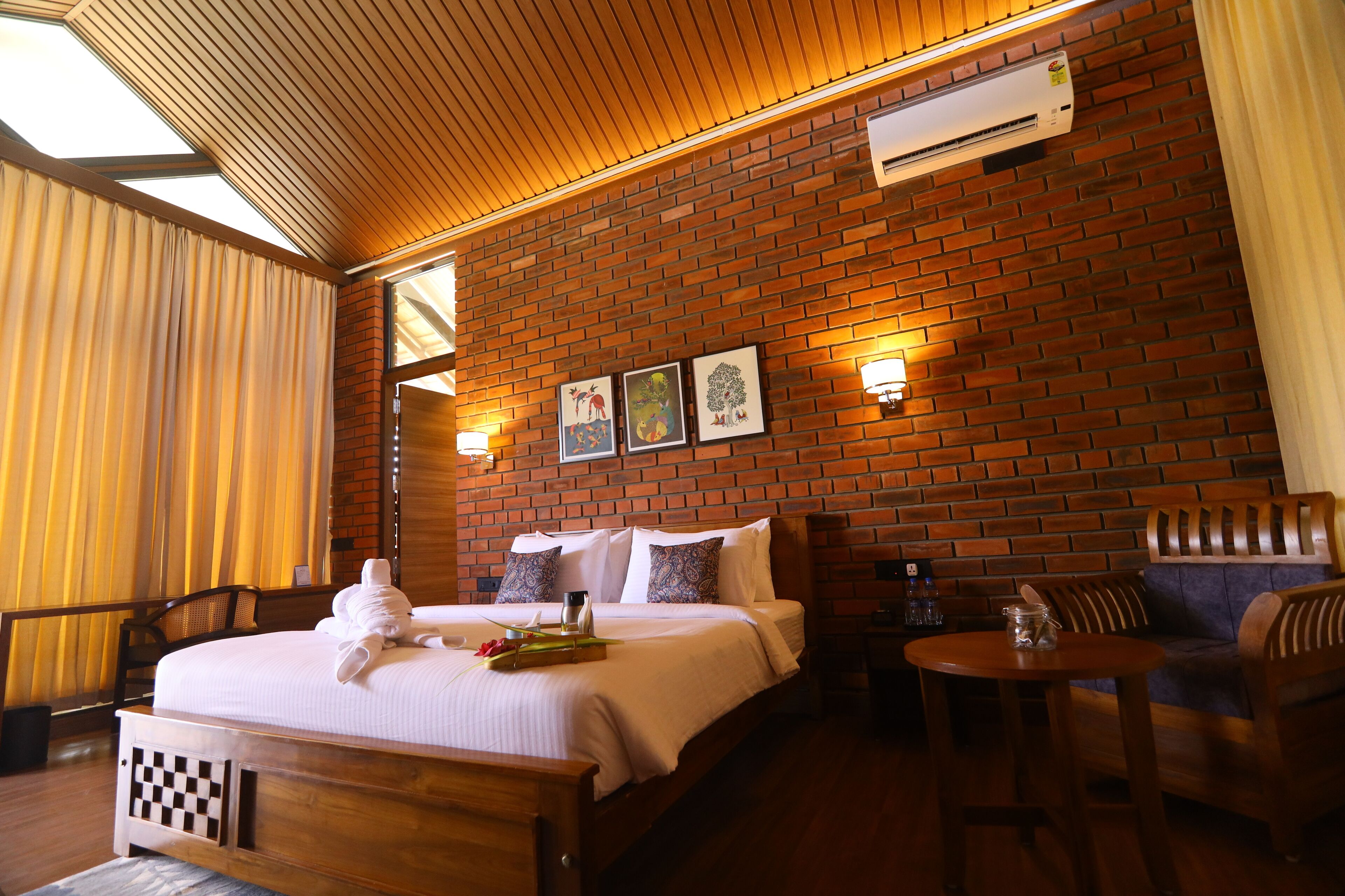 Habitación de hotel con pared de ladrillo, cama con ropa blanca, cabecero de madera, una mesita redonda y una silla.