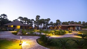 A resort with thatched-roof buildings, a pool, and well-lit pathways. - LA PALMERA (Kadaladi)