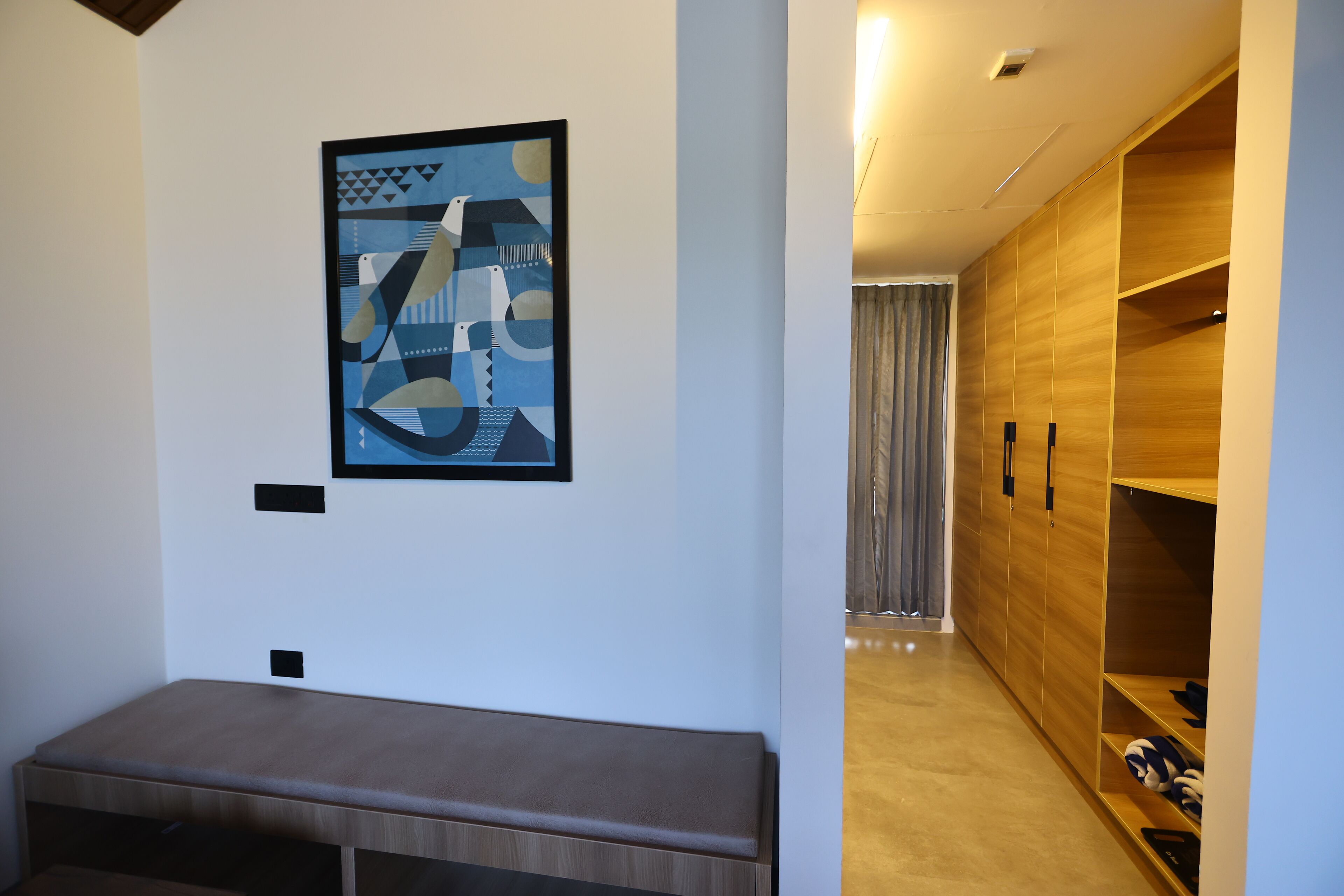 Une chambre moderne avec un banc, une armoire en bois et une œuvre d’art géométrique accrochée au mur.