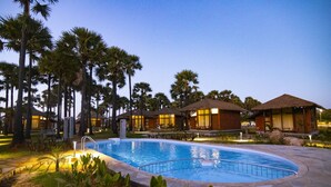 A resort with a swimming pool, palm trees, and thatched-roof buildings. - LA PALMERA (Kadaladi)