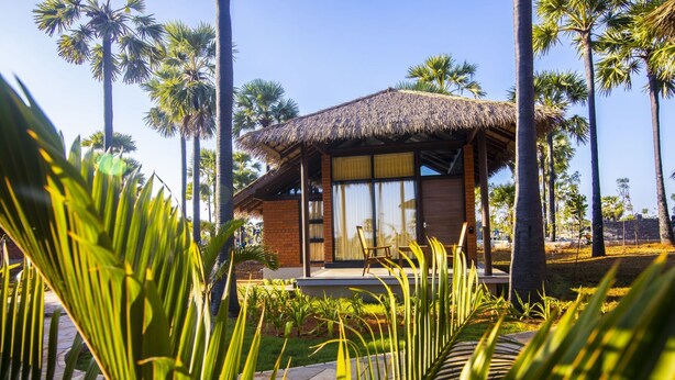 A modern building with a thatched roof, surrounded by palm trees and lush greenery. - LA PALMERA (Kadaladi)